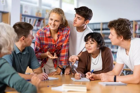 Eine Klassensprecherin, eine weitere Schülerin und drei Schüler unterhalten sich in der Bibliothek angeregt mit ihrer Lehrerin.
