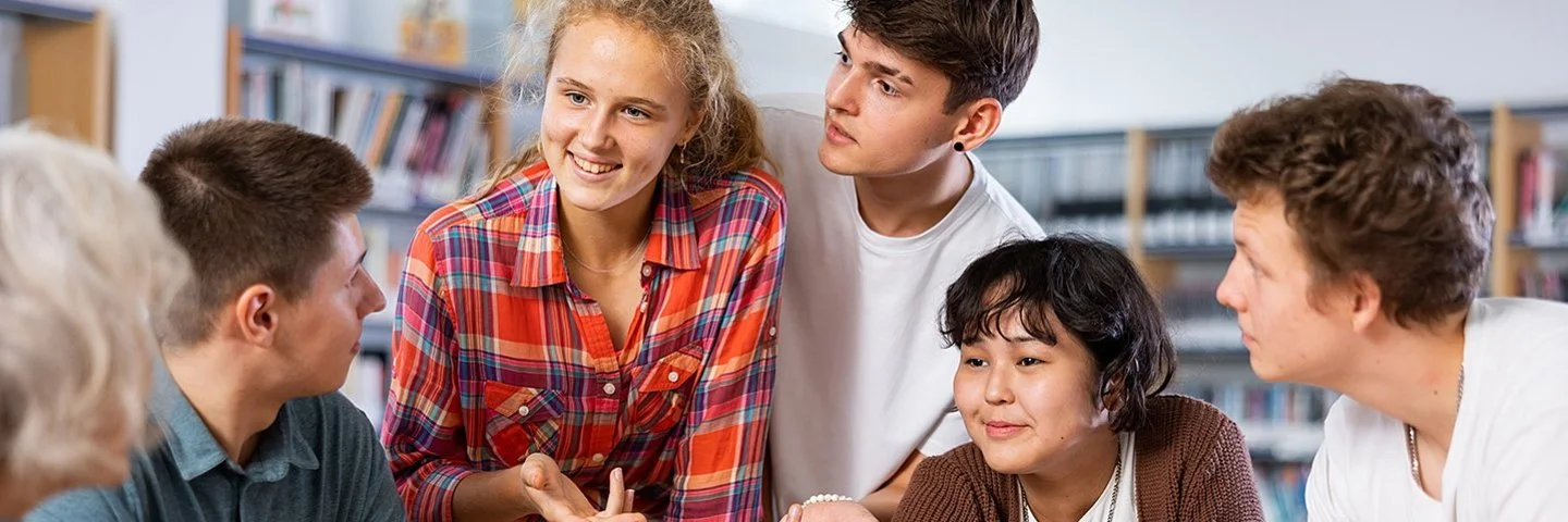 Eine Klassensprecherin, eine weitere Schülerin und drei Schüler unterhalten sich in der Bibliothek angeregt mit ihrer Lehrerin.