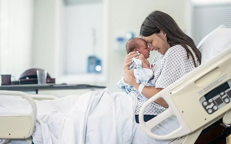 Mutter im Krankenhaus hält ihr Neugeborenes im Arm.