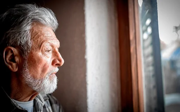 Porträt eines älteren Mannes, der nachdenklich aus dem Fenster schaut.