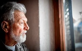 Porträt eines älteren Mannes, der nachdenklich aus dem Fenster schaut.