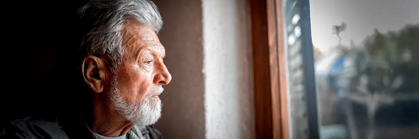 Porträt eines älteren Mannes, der nachdenklich aus dem Fenster schaut.