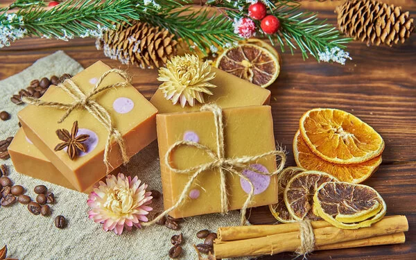 Handgemachte Seifenstücke mit weihnachtlicher Dekoration liegen auf einem Holztisch.