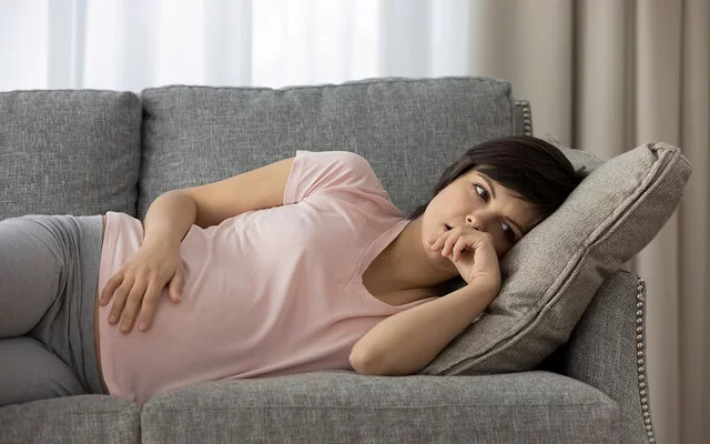 Eine schwangere Frau liegt auf der linken Seite auf der Couch.