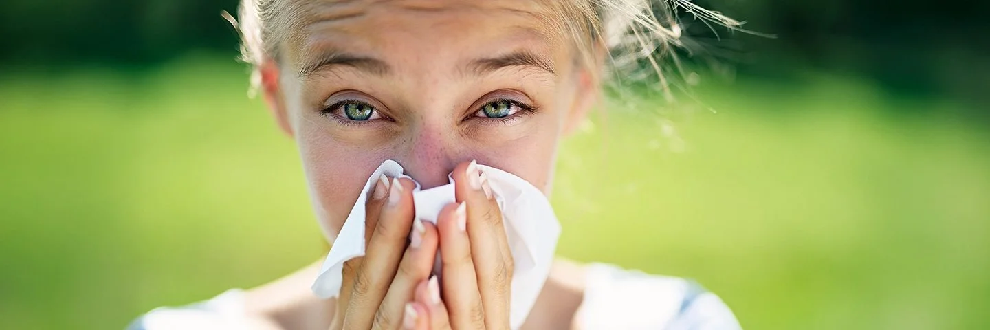 Eine junge Frau putzt sich die Nase mit einem Taschentuch.