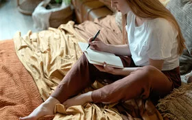 Eine junge Frau sitzt auf dem Bett und notiert sich, welche schlechten Angewohnheiten sie loswerden möchte.