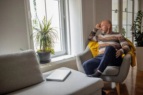 Mann mit Vorerkrankung sitzt lustlos auf einem Sessel und guckt aus dem Fenster.