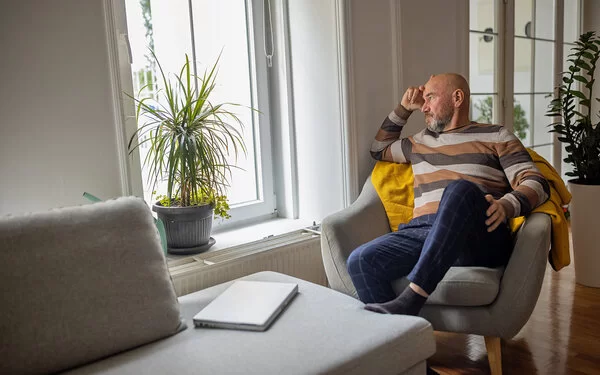 Mann mit Vorerkrankung sitzt lustlos auf einem Sessel und guckt aus dem Fenster.