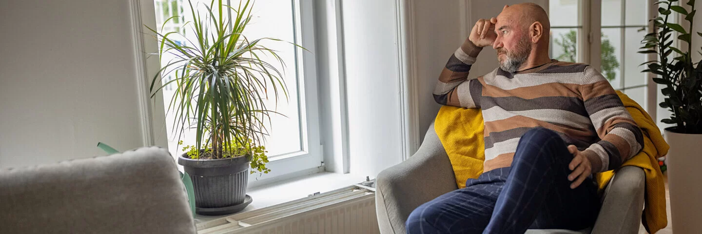 Mann mit Vorerkrankung sitzt lustlos auf einem Sessel und guckt aus dem Fenster.