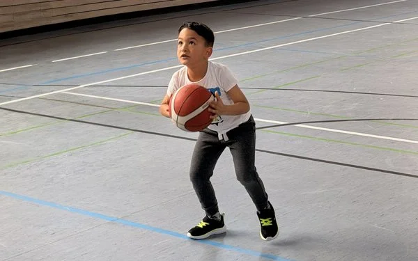Kind trainiert Basketballwurf in einer Sporthalle im Rahmen des Ahorn@school Bewegungs- und Gesundheitsprogramms.