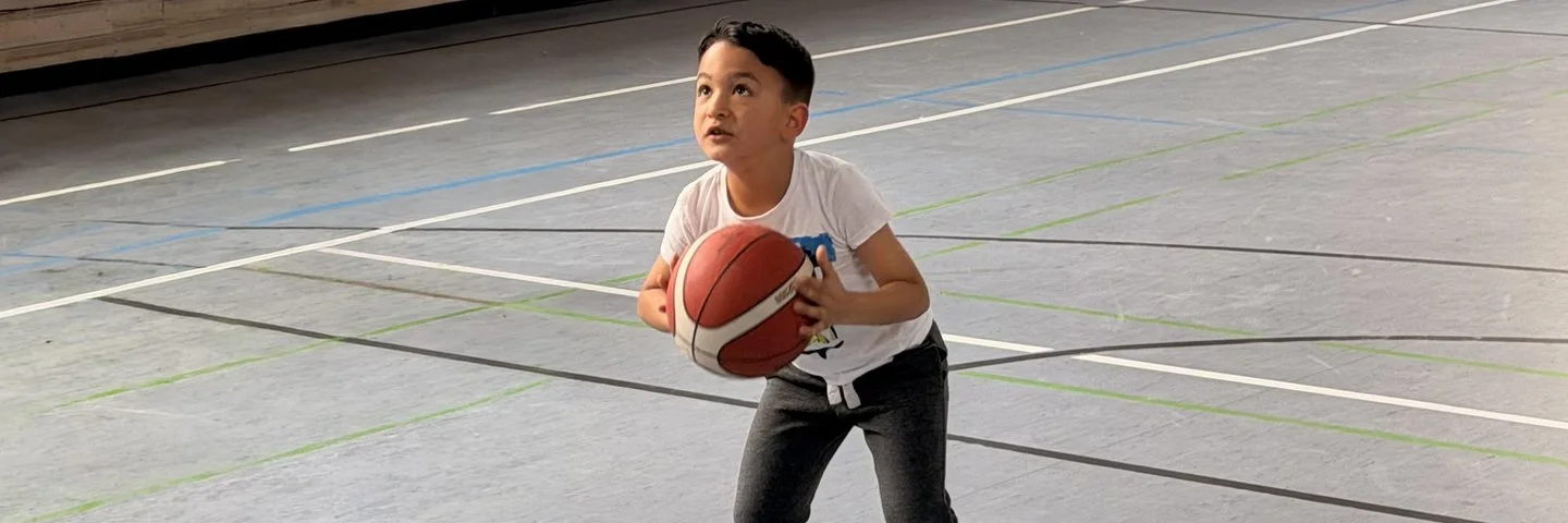 Kind trainiert Basketballwurf in einer Sporthalle im Rahmen des Ahorn@school Bewegungs- und Gesundheitsprogramms.