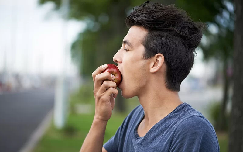 Junger Mann genießt achtsam und bewusst einen Apfel.