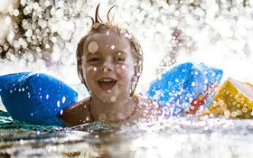 Zwei Kinder planschen im Wasser und tragen Schwimmflügel.