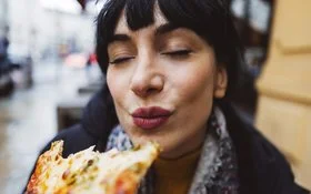 Frau genießt Pizza mit geschlossenen Augen.