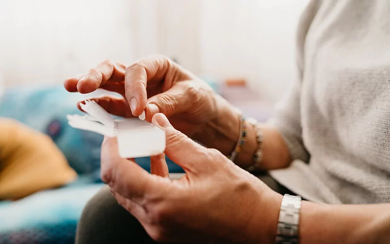 Eine Frau nimmt eine Tablette (ein Gerinnungshemmer) aus einer Medikamentenschachtel.