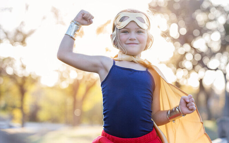 Selbstbewusstsein von Kindern stärken: Mädchen mit gutem Selbstbewusstsein als Superheldin verkleidet.