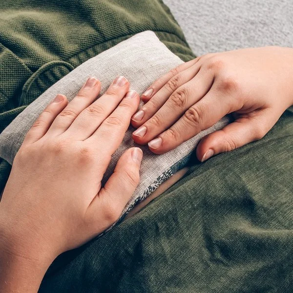 Junge in grünem Pyjama liegt mit einem Wärmekissen auf dem Bauch, das selbst gemacht ist.