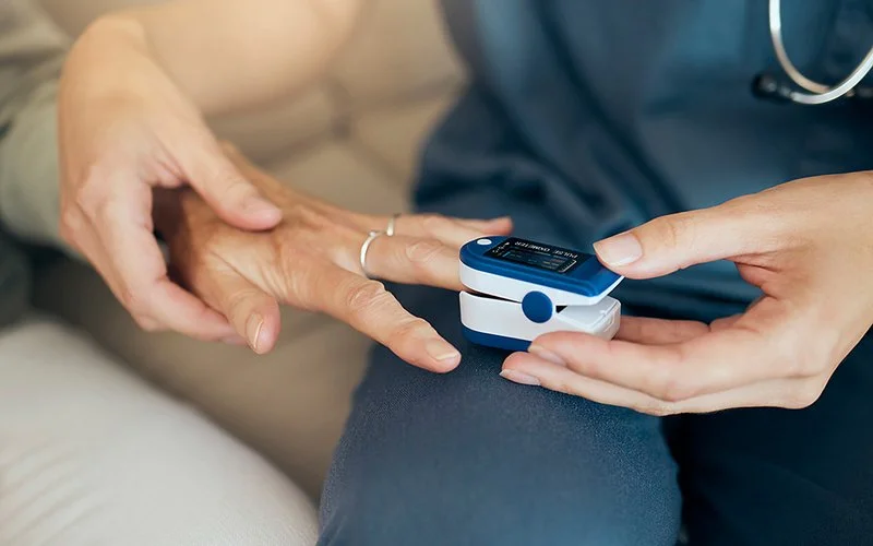 Eine Pflegeperson misst mit einem Oximeter an der Hand einer Patientin den Sauerstoffgehalt der Patientin.