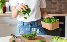 Eine Frau gibt frischen Blattspinat in eine Salatschüssel.