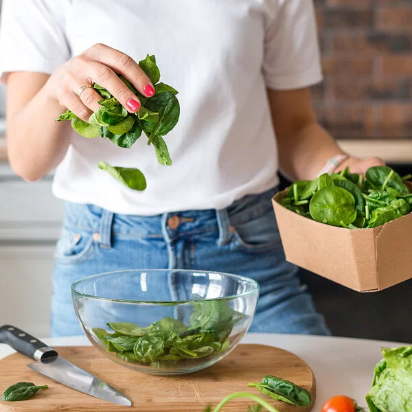 Eine Frau gibt frischen Blattspinat in eine Salatschüssel.