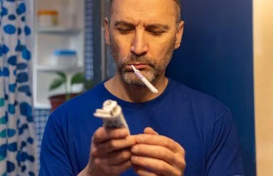 Ein Mann liest beim Zähneputzen im Badezimmer, was auf der Tube der Zahnpasta steht.