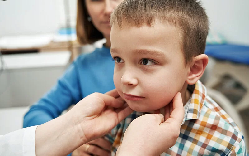 Bei einem Jungen werden in einer Praxis die Lymphknoten am Hals abgetastet.
