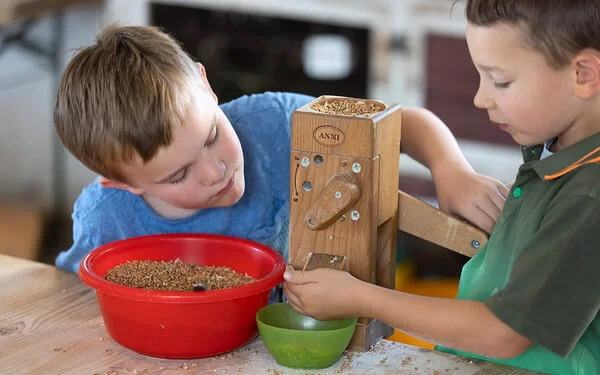 Zwei Jungen mahlen Getreide mit einer Tischmühle.