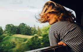 Eine Frau schaut durch das geöffnete Fenster eines fahrenden Zuges.