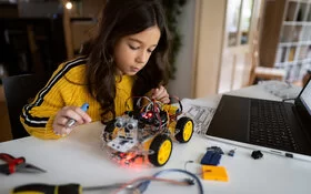 Ein Mädchen bastelt mit Werkzeug an einem Roboterauto.