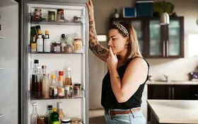 Eine Frau blickt unschlüssig in einen geöffneten Kühlschrank.