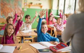 Schüler sitzen in der Klasse und heben die Hand, um dem Lehrer zu antworten.