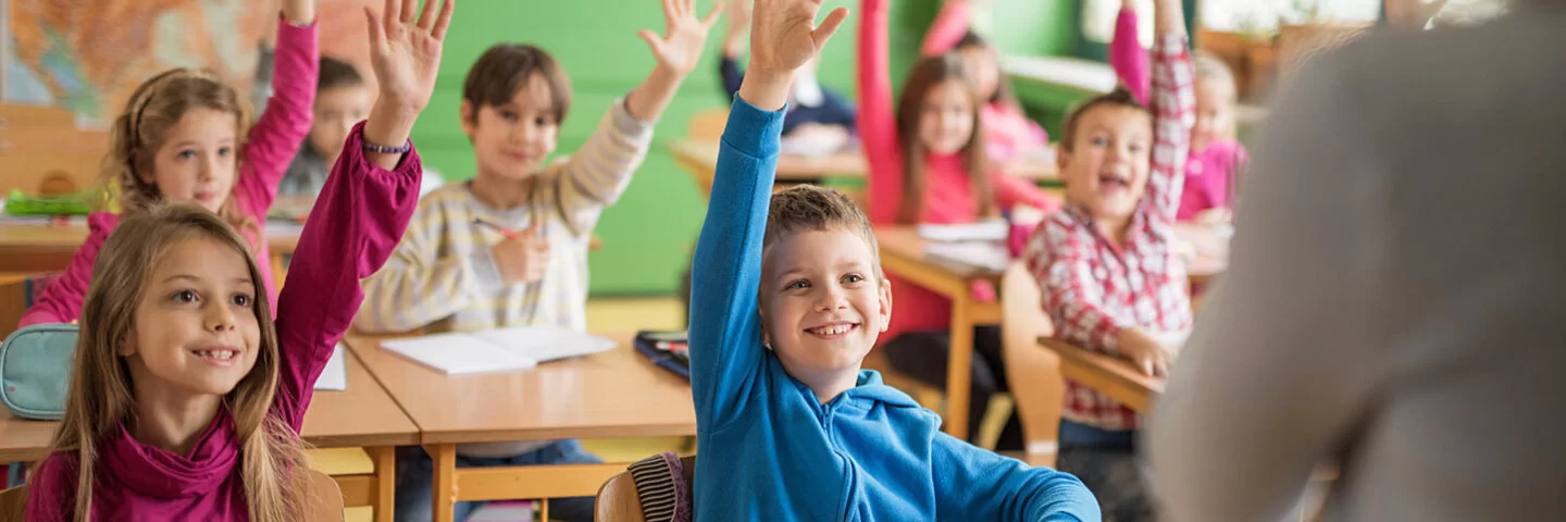 Schüler sitzen in der Klasse und heben die Hand, um dem Lehrer zu antworten.