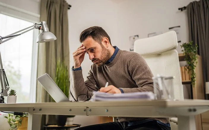 Ein junger Mann sitzt an seinem Schreibtisch und blickt lustlos auf den Bildschirm seines Laptops.