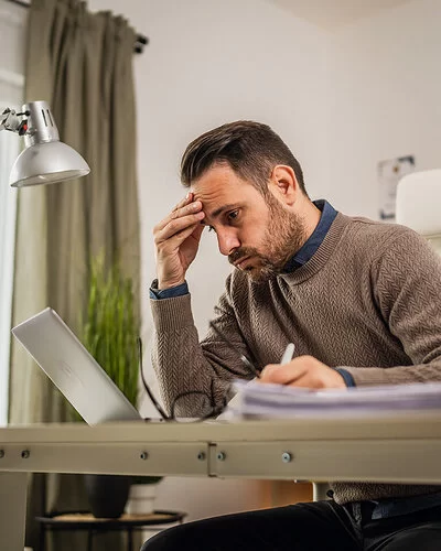 Ein junger Mann sitzt an seinem Schreibtisch und blickt lustlos auf den Bildschirm seines Laptops.