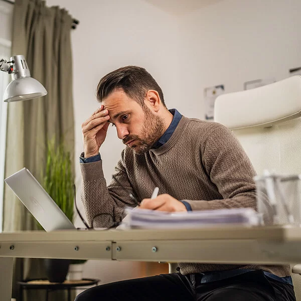 Ein junger Mann sitzt an seinem Schreibtisch und blickt lustlos auf den Bildschirm seines Laptops.