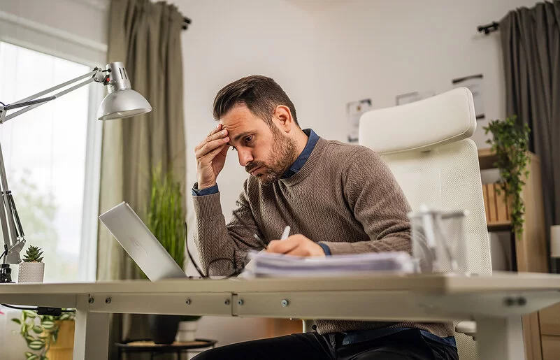Ein junger Mann sitzt an seinem Schreibtisch und blickt lustlos auf den Bildschirm seines Laptops.