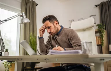 Ein junger Mann sitzt an seinem Schreibtisch und blickt lustlos auf den Bildschirm seines Laptops.