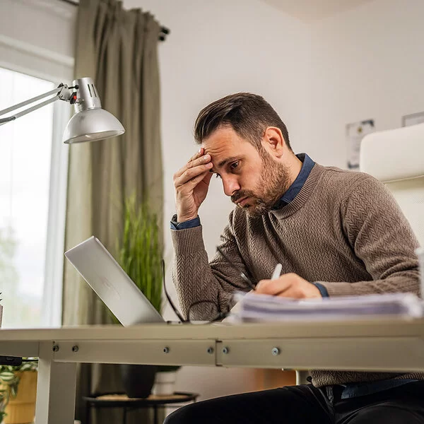 Ein junger Mann sitzt an seinem Schreibtisch und blickt lustlos auf den Bildschirm seines Laptops.