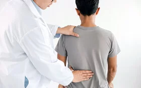 Ein Arzt tastet den unteren Rücken eines Patienten ab.
