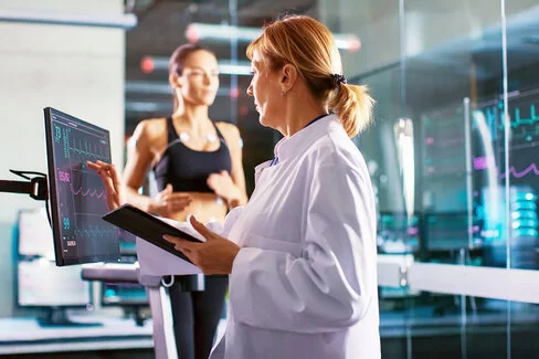 Sportwissenschaftler überprüft den EKG-Status einer Sportlerin, die im Hintergrund auf einem Laufband laufen auf einem Laufband mit Elektroden an ihrem Körper trainiert