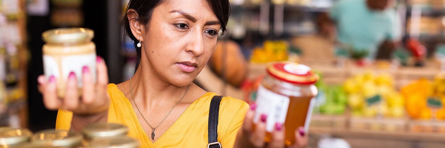 Frau vergleicht beim Einkauf das Mindesthaltbarkeitsdatum von Lebensmitteln.