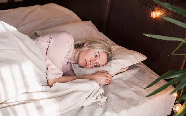 Eine Frau liegt mit offenen Augen im Bett und schaut nachdenklich.