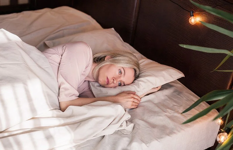 Eine Frau liegt mit offenen Augen im Bett und schaut nachdenklich.