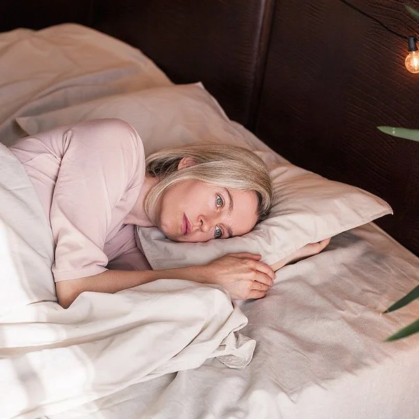 Eine Frau liegt mit offenen Augen im Bett und schaut nachdenklich.