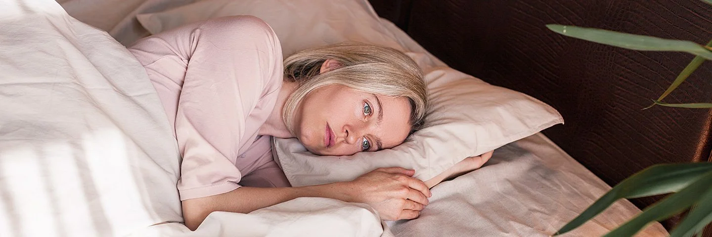 Eine Frau liegt mit offenen Augen im Bett und schaut nachdenklich.