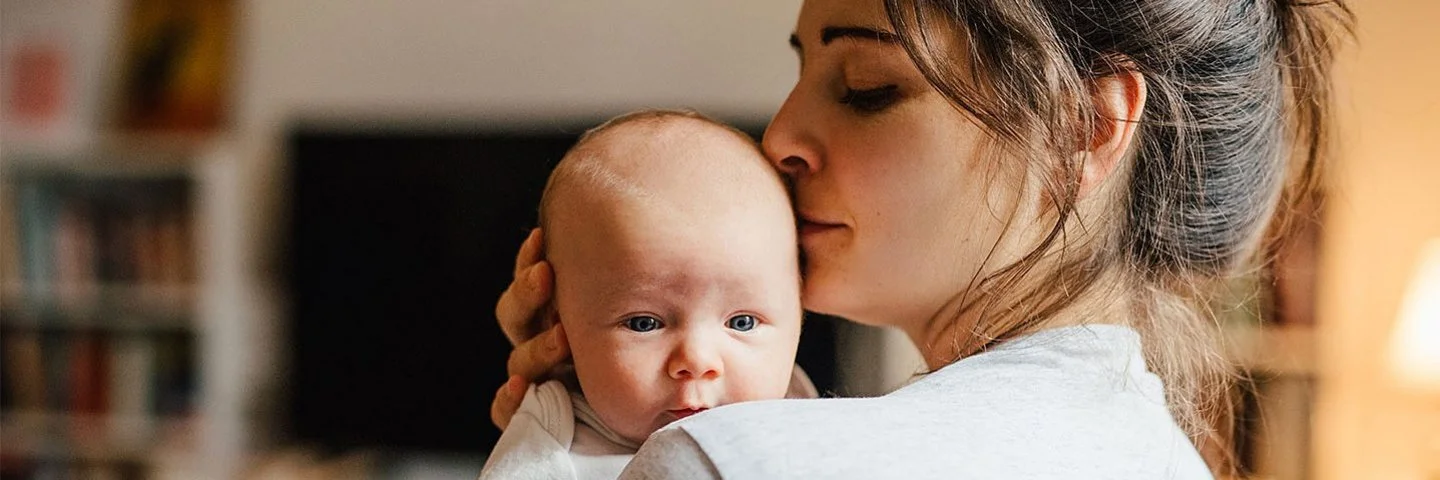 Eine Frau hält ihr Baby auf der Schulter und küsst es sanft