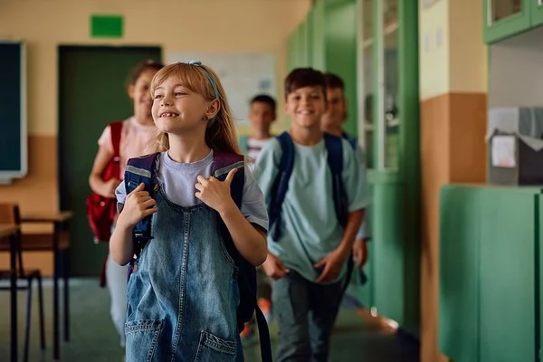 Mehrere Grundschulkinder mit Rucksäcken gehen lachend durch einen Flur.