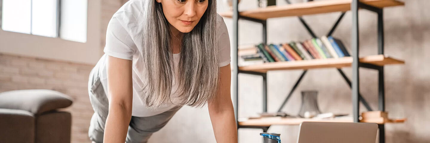 Frau mittleren Alters ist Fitness-Anfängerin und macht ein Workout im Wohnzimmer.