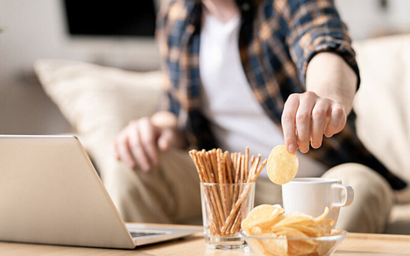 Ein Mann sitzt auf dem Sofa und greift zu einer Schale Chips.