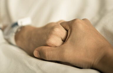 Eine erkrankte Person hält vertrauensvoll die Hände einer Hospiz-Kraft.